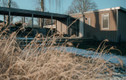 Et moderne lodgehus med træfacade og store vinduer, omgivet af tørt græs og et dækket terrasseområde.
