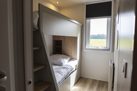Acogedora habitación de un lodge con litera, ventana con vistas al campo y suelo de madera.