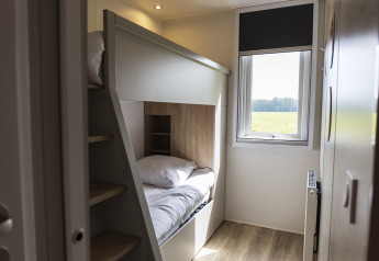 Cozy lodge bedroom featuring a bunk bed, large window with view of fields, and wooden flooring.
