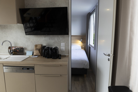 Moderne lodge-keuken met spoelbak, vaatwasser, tv en zicht op een slaapkamer met eenpersoonsbed.