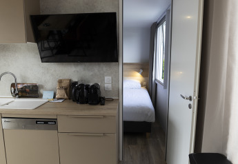 Moderne Lodge mit Küchenzeile, Geschirrspüler, TV und Blick ins Schlafzimmer mit Einzelbett.