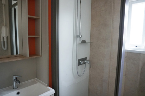 Baño moderno de una cabaña con ducha, lavabo, espejo y estanterías abiertas en tonos claros.