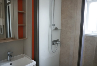 Baño moderno de una cabaña con ducha, lavabo, espejo y estanterías abiertas en tonos claros.