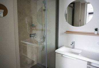 Modernes Badezimmer mit Dusche, Waschbecken, rundem Spiegel und Pflanze in der Family lodge De Boshoek.