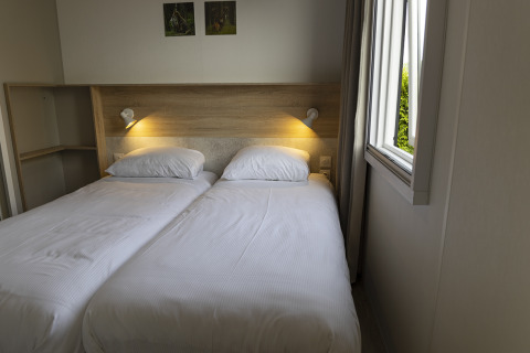 Familielodge med to enkeltsenge og åbent vindue i Holiday park De Boshoek, Holland, indbydende værelse.