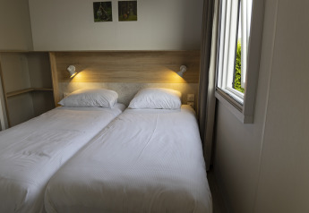 Familielodge med to enkeltsenge og åbent vindue i Holiday park De Boshoek, Holland, indbydende værelse.