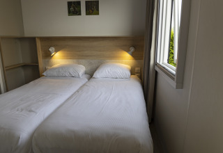Familielodge met twee eenpersoonsbedden en een open raam in Holiday park De Boshoek, Nederland.