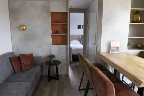 Interior de una cabaña moderna con sala, comedor y dormitorio visible al fondo, decoración elegante.