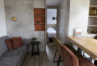 Interior de una cabaña moderna con sala, comedor y dormitorio visible al fondo, decoración elegante.