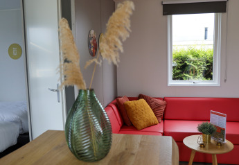 Gezellige Family Lodge zithoek met rode zetel, groene vaas en kussens bij De Boshoek vakantiepark.