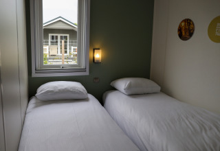 Gemütliches Zimmer mit zwei Einzelbetten, Wandlampe, Fenster und Blick auf das Nachbarhaus in De Boshoek.