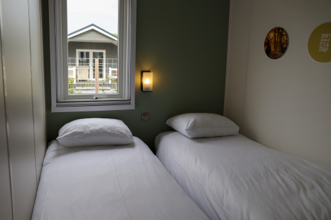 Chambre confortable avec deux lits simples, fenêtre et vue sur une maison voisine à Family Lodge, De Boshoek.
