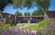 Lodge familiar en Holiday park De Boshoek, Países Bajos, con flores, vegetación y terraza exterior cubierta.