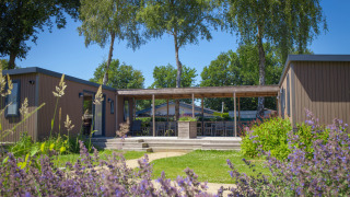 Familien-Lodge im Holiday Park De Boshoek, Niederlande, mit Terrasse, Blumen und umgeben von grüner Natur.