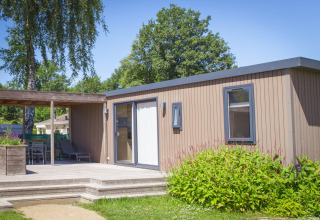 Family lodge presso Holiday park De Boshoek, Paesi Bassi, con patio in legno e giardino verde.