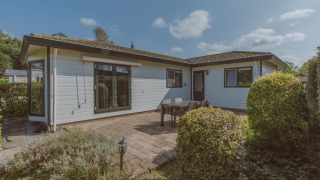 Außenansicht des Wilbrink-Chalets im Ferienpark De Boshoek, mit Terrasse, Tisch und grünen Büschen.