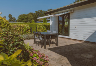 Outdoor terrace with black table and chairs at Wilbrink chalet, Holiday park De Boshoek, Netherlands, garden view.
