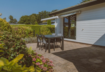Outdoor terrace with black table and chairs at Wilbrink chalet, Holiday park De Boshoek, Netherlands, garden view.