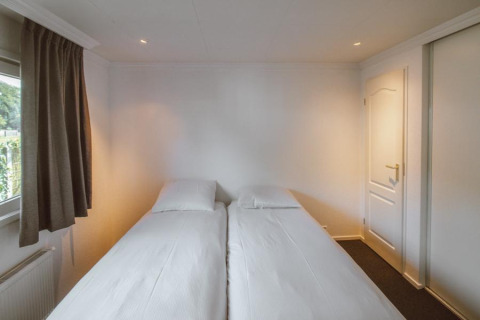 Dormitorio luminoso con dos camas individuales en el chalet Wilbrink de Holiday park De Boshoek, Países Bajos.