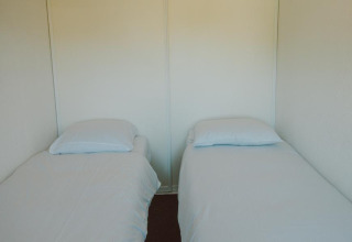 Dos camas individuales con sábanas y almohadas blancas en el Wilbrink chalet de Holiday park De Boshoek.
