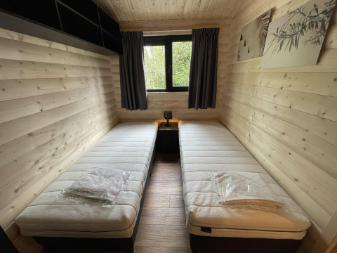 Een kamer in Hackfort Wood 6 lodge op De Utrechtse Heuvelrug, Nederland, met twee aparte bedden en houten muren.