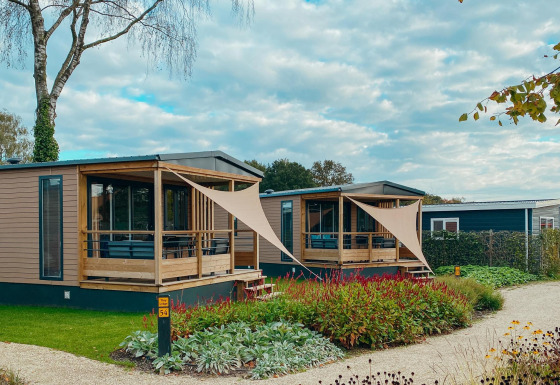 Two Tiny Court lodges at Holiday park De Boshoek in the Netherlands, featuring wooden decks and gardens.