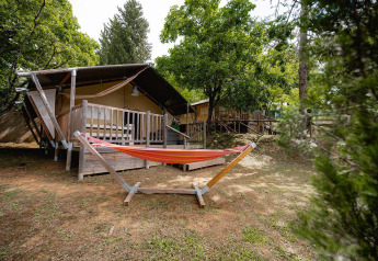 Safari-Zelt Villatent Wood mit Veranda und Hängematte auf Camping Colleverde, von Bäumen umgeben in Italien.