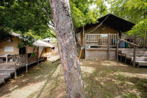 Tende safari al Camping Colleverde in Italia con terrazza in legno, circondate da alberi verdi.