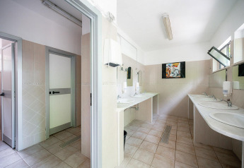 Baño con varios lavabos, espejos y cabinas privadas en Villatent Wood, Camping Colleverde, Italia.