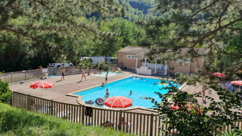 Piscina y zona de recreo en Camping Le Gallo Romain, rodeada de árboles y personas, en Auvergne-Rhône-Alpes, Francia.