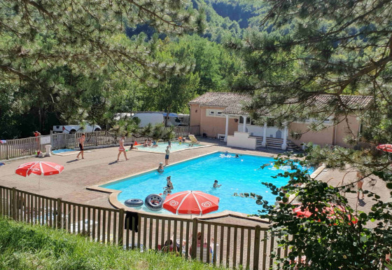 Swimmingpool og ferieområde med gæster ved Camping Le Gallo Romain, omgivet af grønne træer i Auvergne-Rhône-Alpes.