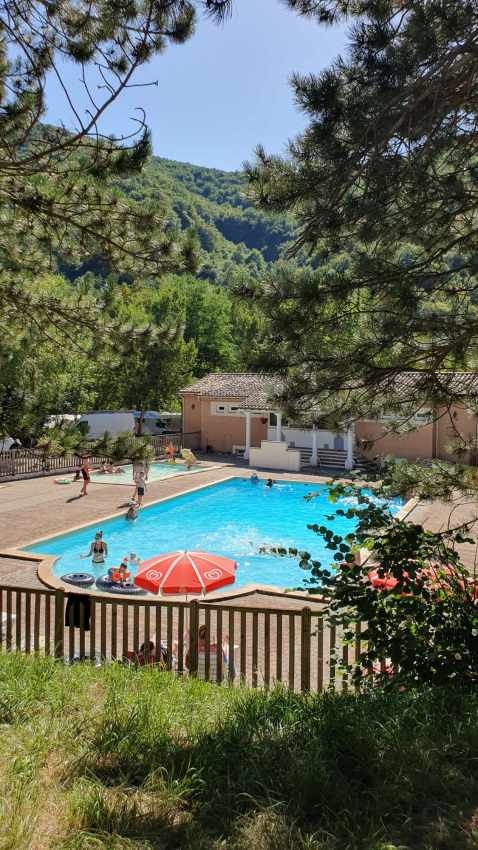 Vista de la piscina en Camping Le Gallo Romain, rodeada de colinas verdes en Auvergne-Rhône-Alpes, Francia.