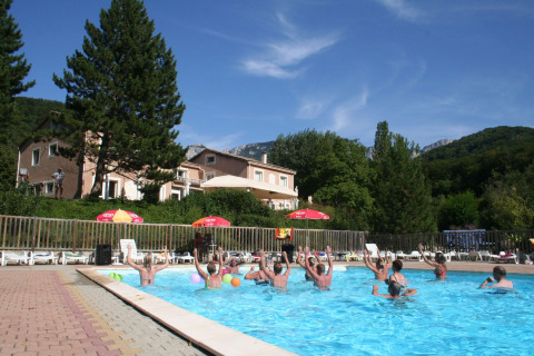 Personas haciendo aeróbic acuático en la piscina de Camping Le Gallo Romain con montañas al fondo.
