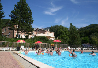 Gruppe mennesker laver vandaerobic i swimmingpool på Camping Le Gallo Romain med bjerge i baggrunden.
