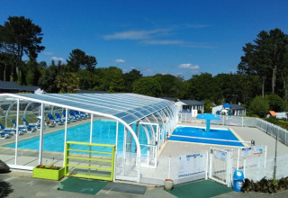 Udendørs swimmingpool og overdækket poolområde ved Camping de Kerleyou, omgivet af grønt i Bretagne, Frankrig.
