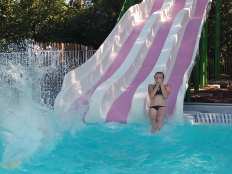 Una persona scende da uno scivolo rosa e bianco in piscina al Camping lac Aux Oiseaux in Occitania, Francia.