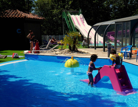 Niños juegan en la piscina con un tobogán en Camping lac Aux Oiseaux, un parque vacacional en Occitania, Francia.