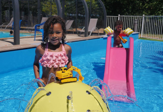 Bambini che giocano in piscina con escavatori giocattolo, scivolo rosa e getti d’acqua al Camping lac Aux Oiseaux.