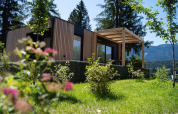Modern Enzian lodge with wooden exterior and pergola, nestled among greenery and mountains in nature.