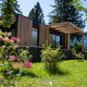 Et moderne Enzian-lodge med træfacade og terrasse, omgivet af grønne planter i naturskønne omgivelser.