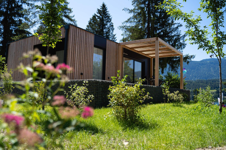 Moderno lodge Enzian con fachada de madera y terraza, rodeado de vegetación y montañas hermosas.