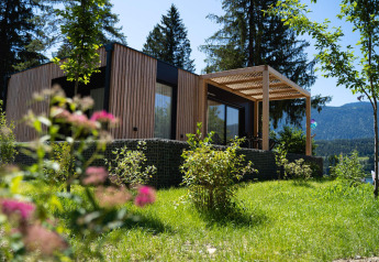 Moderno lodge Enzian con fachada de madera y terraza, rodeado de vegetación y montañas hermosas.