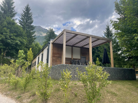 Lodge moderne Enzian près du lac Pressegger See en Autriche, entourée d’arbres et de montagnes sous un ciel nuageux.