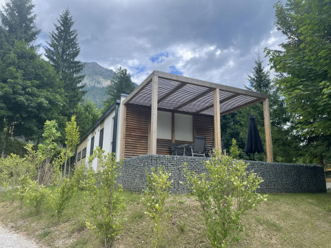 Cabaña moderna Enzian en Pressegger See, Austria, rodeada de árboles y montañas bajo un cielo nublado.