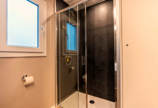 Salle de bain moderne avec douche vitrée, grande fenêtre et porte-papier à Enzian, Pressegger See, Autriche.