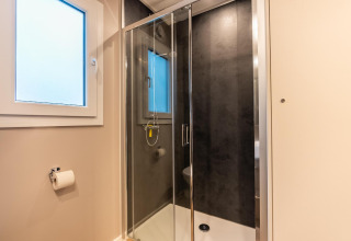 Baño moderno con cabina de ducha de vidrio, ventana grande y portapapel en Enzian, Pressegger See, Austria.