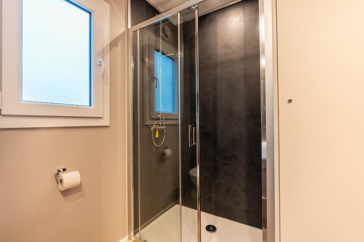 Baño moderno con cabina de ducha de vidrio, ventana grande y portapapel en Enzian, Pressegger See, Austria.