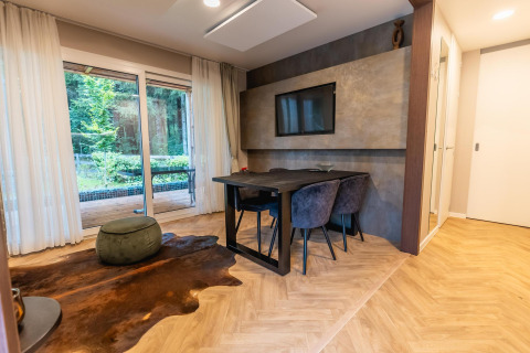 Moderne lodge aan het Pressegger See in Oostenrijk met glazen deuren, eettafel en televisiescherm aan de muur.