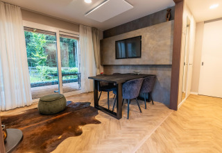 Moderne lodge aan het Pressegger See in Oostenrijk met glazen deuren, eettafel en televisiescherm aan de muur.