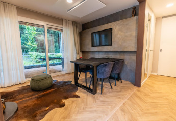 Moderne lodge ved Pressegger See i Østrig med glasdøre til terrasse, spisebord og fladskærms-tv på væggen.